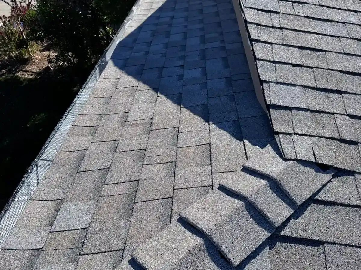 Close-up of damaged and lifted asphalt shingles on a residential roof during inspection