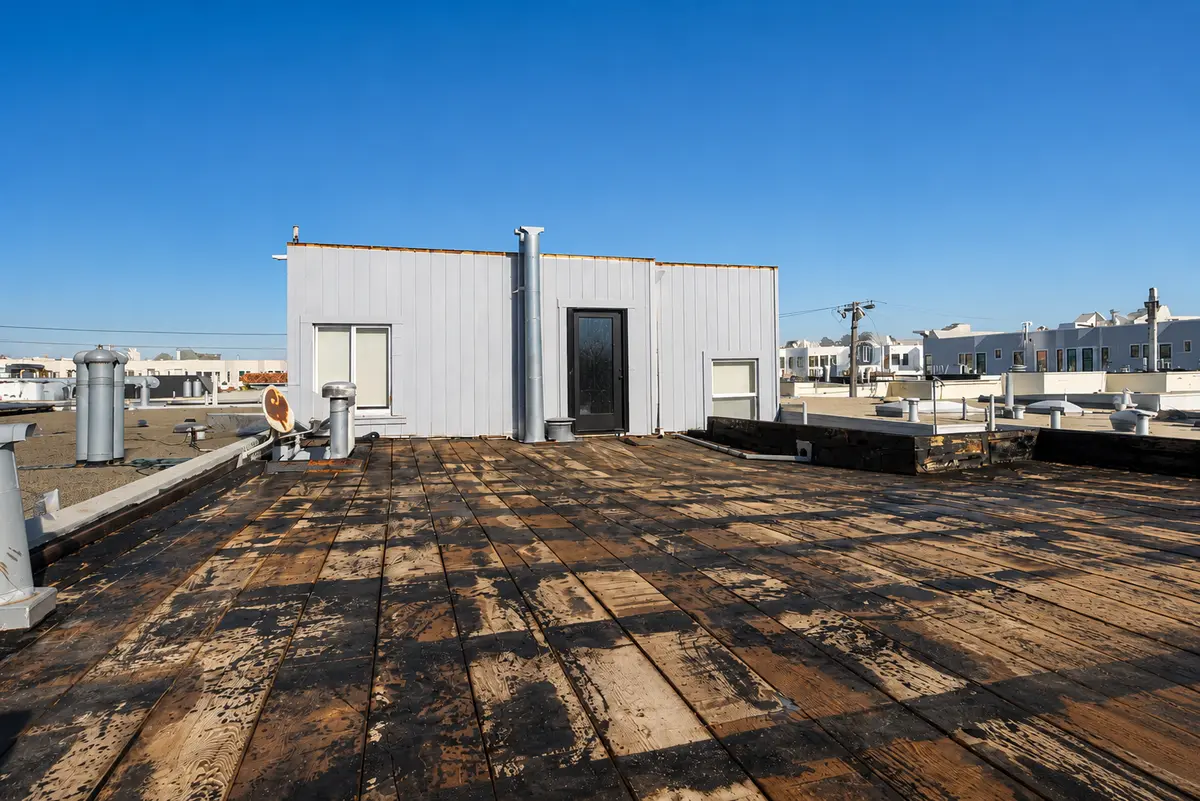 Deteriorated flat roof showing severely weathered and blackened exposed wood deck planking with peeling membrane remnants, indicating a flat roof system well past its service life and in need of full replacement.