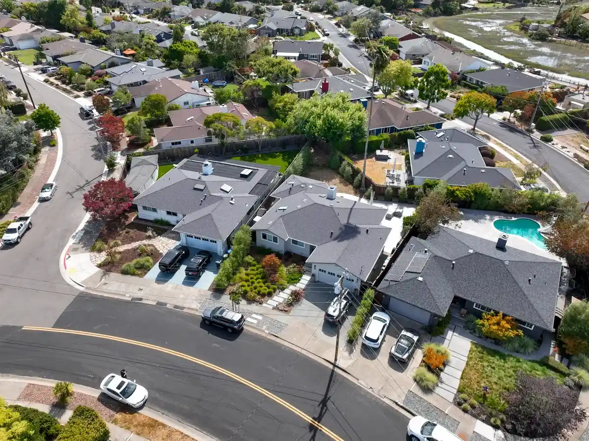 Aerial view of a Marin County residential street with gray asphalt shingle roofs on single-story homes beside a tidal marsh.