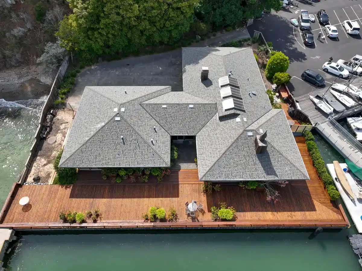 Aerial view of a gray asphalt shingle hip roof with clusters of box vents and skylights on a waterfront home