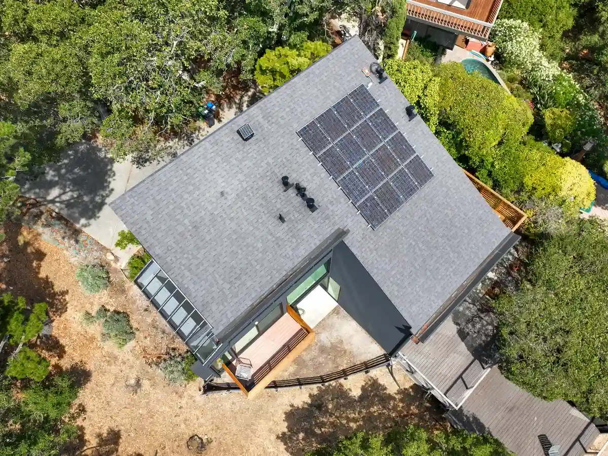 Top-down view of an asphalt shingle roof with a box vent near the peak, pipe vents, and solar panels.
