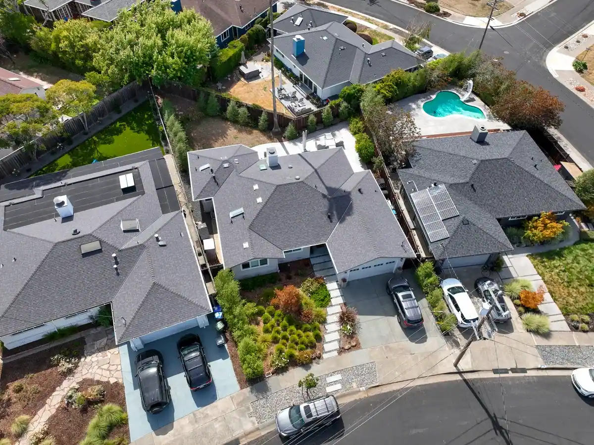 Aerial view of single-family homes with gray asphalt shingle roofs, skylights, and roof vents in a residential neighborhood.